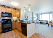 Thumbnail 17 of 104 - A kitchen with a black oven and microwave, wooden cabinets, and a rug on the floor at The Grand Apartments, Oakland 94612