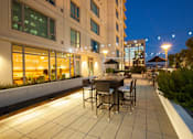 Thumbnail 7 of 104 - A patio with a table and chairs is lit up at night at The Grand Apartments, California, 94612