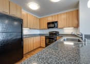 Thumbnail 18 of 104 - A black refrigerator is in a kitchen with wooden cabinets at The Grand Apartments, Oakland