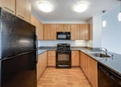 Thumbnail 20 of 104 - A black fridge in a kitchen with wooden cabinets at The Grand Apartments, California, 94612