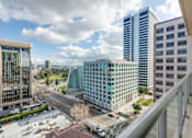 Thumbnail 2 of 104 - A cityscape with a mix of modern and older buildings, a clear sky, and a parking lot in the foreground at The Grand Apartments, Oakland, California