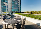 Thumbnail 9 of 104 - A wooden table and chairs are on a patio with a building in the background at The Grand Apartments, California