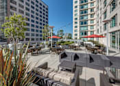 Thumbnail 96 of 104 - A patio with tables and chairs is surrounded by buildings at The Grand Apartments, Oakland