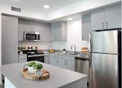 Thumbnail 41 of 87 - A modern kitchen with a stainless steel refrigerator and a wooden tray with two potted plants on the counter.