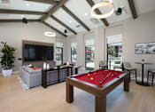 Thumbnail 6 of 87 - A pool table is in the middle of a room with a couch, chairs, and a television.
