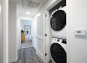Thumbnail 52 of 87 - A white washing machine is in a small room with a door open.