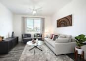 Thumbnail 44 of 87 - A living room with a grey couch, a coffee table, a fan, and a painting on the wall.