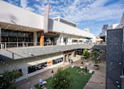 Thumbnail 84 of 85 - A view of a shopping mall with a green lawn and people walking around.