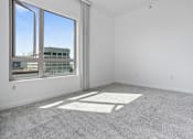 Thumbnail 72 of 104 - A large empty room with a carpeted floor and a large window at The Grand Apartments, Oakland, CA