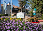 Thumbnail 3 of 81 - Property entrance sign with colorful landscaping at Woodbend Apartments, Alta Loma, California