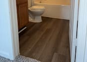 Thumbnail 15 of 16 - A white toilet is in a bathroom with wood flooring.