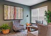Thumbnail 2 of 10 - A living room with a grey chair, a brown chair, a small table, and a potted plant.