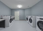 Thumbnail 9 of 38 - A row of washing machines are lined up in a laundry room.