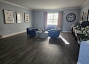 Thumbnail 5 of 14 - A living room with a grey wall and a large clock on the wall.