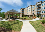 Thumbnail 21 of 38 - A gazebo is surrounded by a grassy area in front of apartment buildings.