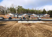 Thumbnail 6 of 8 - A parking lot in front of a building with a tree in the middle.