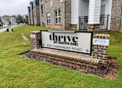 Thumbnail 9 of 10 - A brick sign that says Thrive at South End stands in front of a building.