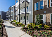 Thumbnail 13 of 13 - A modern apartment complex with a walkway and landscaping.