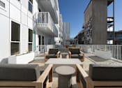 Thumbnail 4 of 13 - A modern outdoor seating area with white walls and wooden furniture.