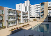 Thumbnail 3 of 13 - A modern apartment complex with a pool in the foreground.