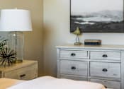 Thumbnail 14 of 53 - A bedroom with a bed, nightstand, and a large picture on the wall.
