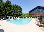 Thumbnail 5 of 14 - A pool surrounded by trees and chairs at Ballantyne Commons of Stockbridge Apartments, Stockbridge, GA