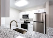 Thumbnail 6 of 14 - A kitchen with a granite countertop and stainless steel appliances at Ballantyne Commons of Stockbridge Apartments, Stockbridge