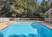 Thumbnail 16 of 20 - A blue swimming pool surrounded by a white fence and trees at The Madison Apartments and Townhomes, Lawrenceville, 30044