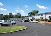 Thumbnail 2 of 20 - A parking lot with cars and a building in the background at The Madison Apartments and Townhomes, Lawrenceville, GA