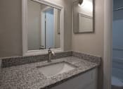 Thumbnail 8 of 20 - A bathroom sink with a granite countertop and a mirror above it at The Madison Apartments and Townhomes, Lawrenceville, 30044