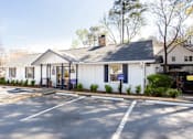 Thumbnail 15 of 27 - A white building with a black roof is surrounded by a parking lot at Barcelo at East Cobb Apartments, Marietta, GA