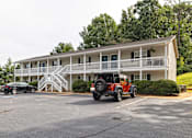 Thumbnail 11 of 14 - A red car is parked in front of a white building with a black car parked behind it at Overlook Club Apartments, Cummings