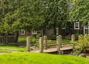 Thumbnail 47 of 48 - A wooden bridge over a grassy area with a house in the background.