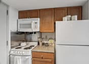 Thumbnail 22 of 25 - A white refrigerator stands in a kitchen with wooden cabinets.