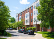 Thumbnail 10 of 17 - a brick and white apartment building with cars parked in front of it