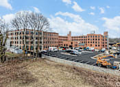 Thumbnail 8 of 27 - A large red brick building with a parking lot in front.
