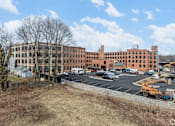 Thumbnail 21 of 27 - A large red brick building with a parking lot in front.