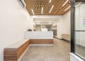 Thumbnail 2 of 2 - A reception area with a white counter and a wooden bench.