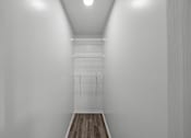 Thumbnail 12 of 17 - A white room with a wooden floor and a white closet with a shelf and hangers.