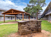 Thumbnail 10 of 15 - A wooden pavilion is in the middle of a grassy area with a stone pillar in the foreground.