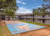 Thumbnail 13 of 15 - A mural of a woman is painted on a concrete surface in front of apartment buildings.