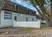 Thumbnail 11 of 19 - A white building with a sign that says "Legacy Lofts" is for lease.