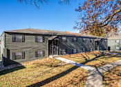 Thumbnail 1 of 27 - A large grey building with a brown roof and a white walkway in front.