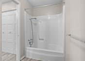 Thumbnail 10 of 15 - A white bathtub with a shower head and a white door.