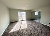 Thumbnail 1 of 28 - A large empty room with a carpeted floor and a view of a balcony through the door.