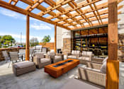 Thumbnail 6 of 25 - A wooden pergola over a patio with wicker furniture.
