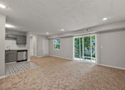 Thumbnail 10 of 20 - A spacious room with a carpeted floor and sliding glass doors leading to a backyard.
