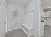 Thumbnail 13 of 52 - A white room with a bench and a door leading to another room.