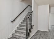 Thumbnail 26 of 32 - A staircase with a metal railing and a carpeted runner.