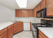 Thumbnail 3 of 13 - A kitchen with wooden cabinets and a black microwave above the stove.